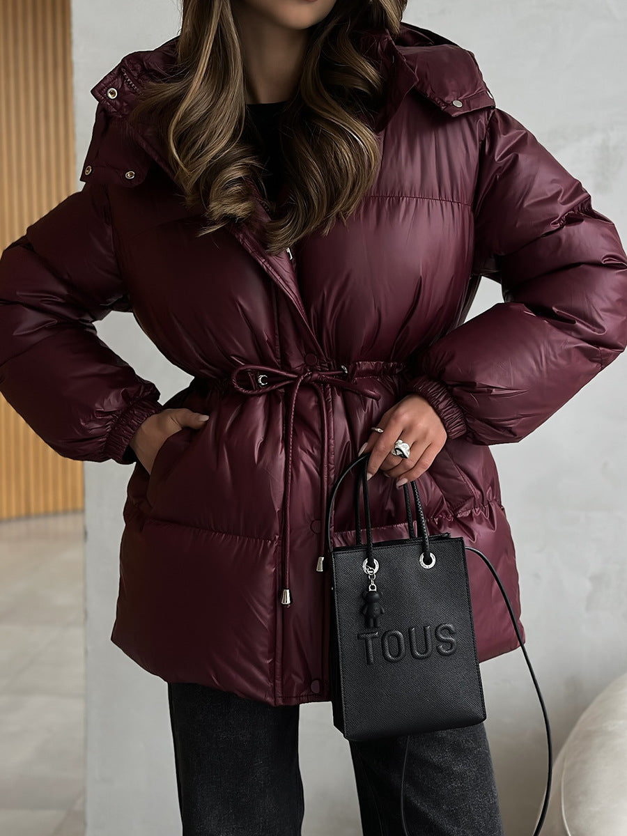Person wearing a maroon puffer coat holding a black handbag with 'Tous' branding.