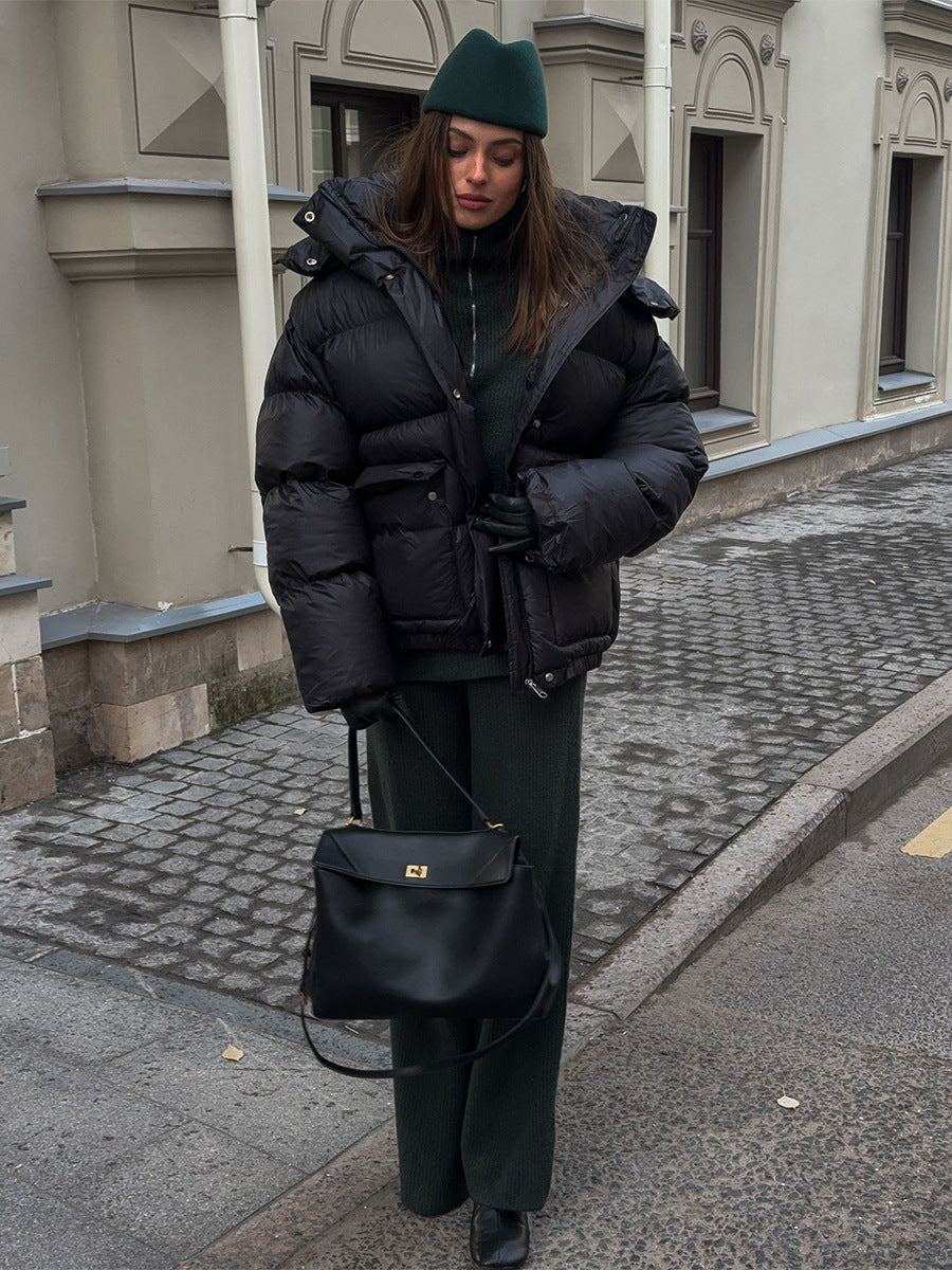Person wearing a black puffer jacket and green beanie walking on a street.