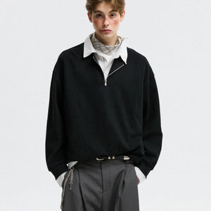 Person wearing a black sweater over a white shirt with gray pants on a light gray background