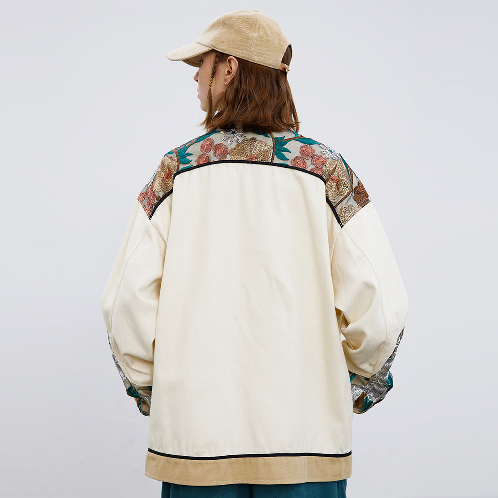 Person wearing a cream-colored jacket with floral patterns on sleeves against a white background