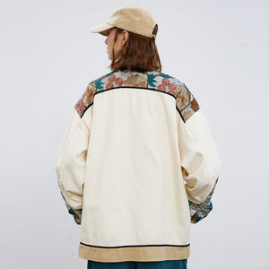 Person wearing a cream-colored jacket with floral patterns on sleeves against a white background
