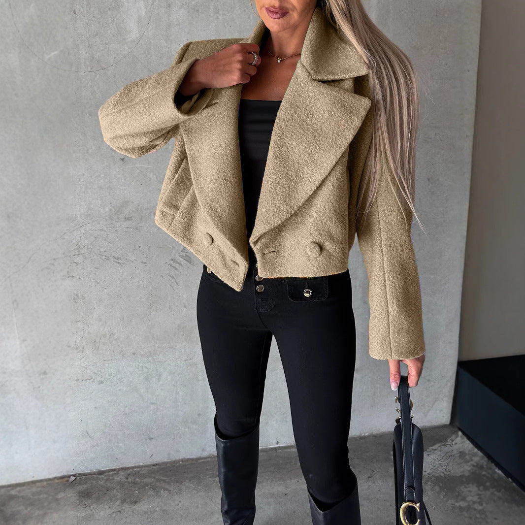 Woman wearing a beige coat and black pants against a gray wall.