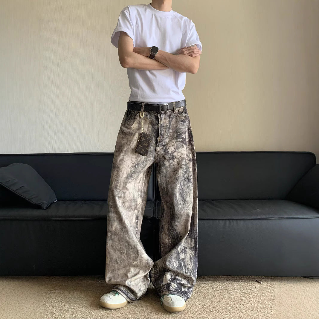 Person wearing a white t-shirt and distressed jeans standing in a room with a black sofa.