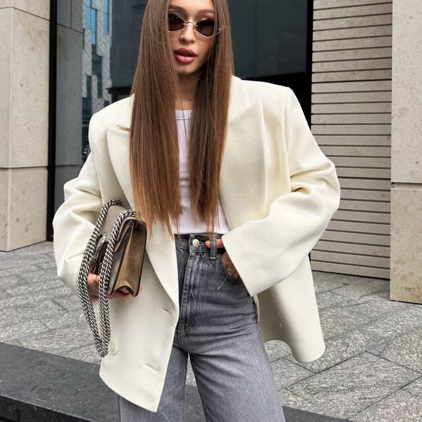 Woman wearing a white coat and gray pants, holding a handbag on a city street.