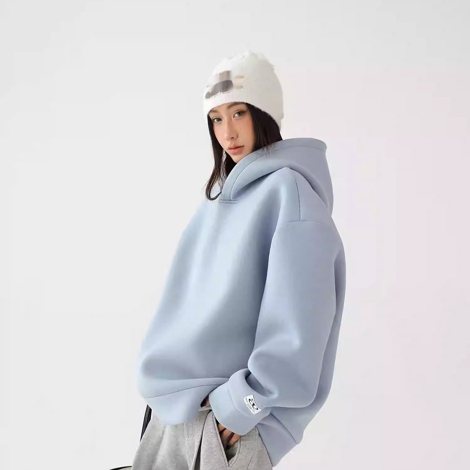 Person wearing a light blue hoodie and white beanie on a plain background