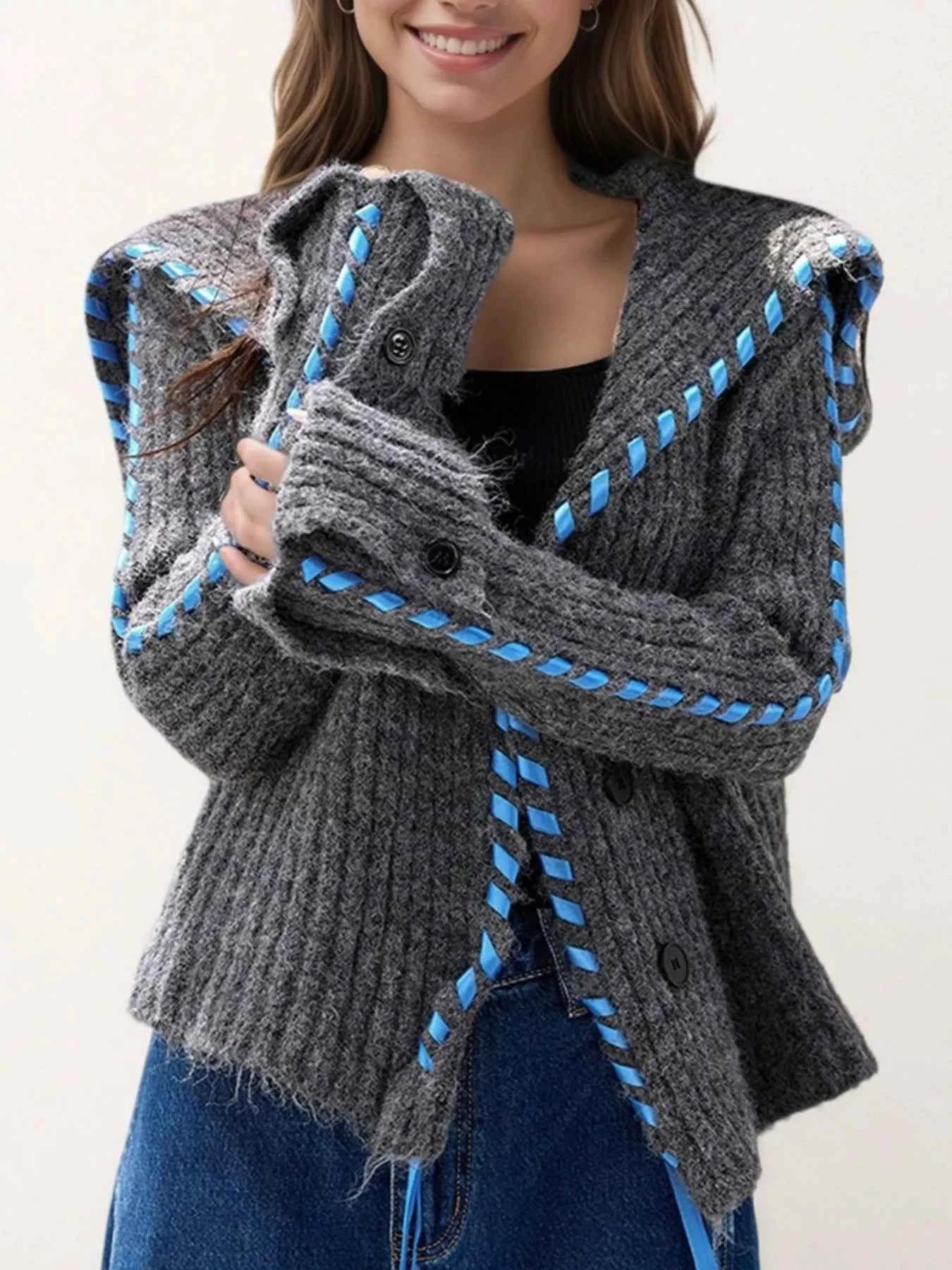 Person wearing a gray knit cardigan with blue accents on a plain background