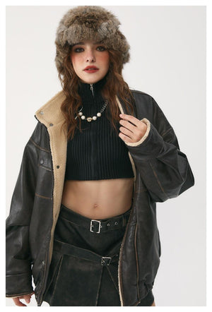 A person wearing a winter coat with a stand collar, large patch pockets, and a belt. The coat is unbuttoned, revealing a turtleneck underneath.