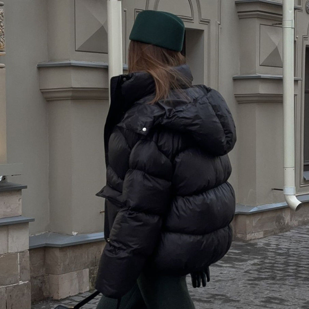 Person wearing a black puffer jacket and green cap walking away from the camera on a street.