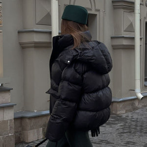 Person wearing a black puffer jacket and green cap walking away from the camera on a street.