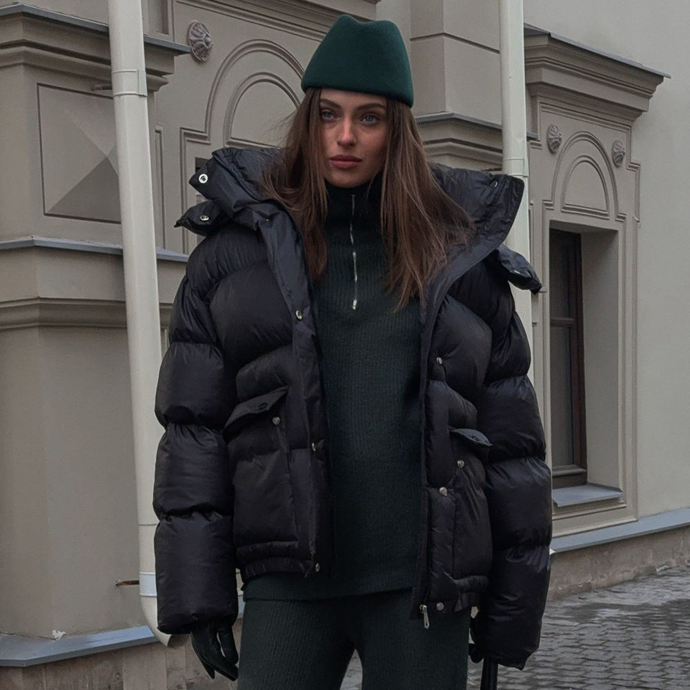 Person wearing a black puffer jacket and green beanie standing in front of a building.
