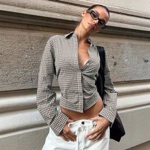 Woman wearing a checkered shirt and white pants against a textured wall.