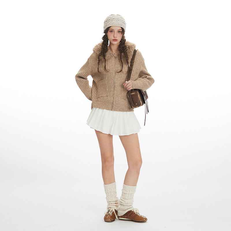 Person wearing a brown knitted sweater, white skirt, and beige boots on a white background