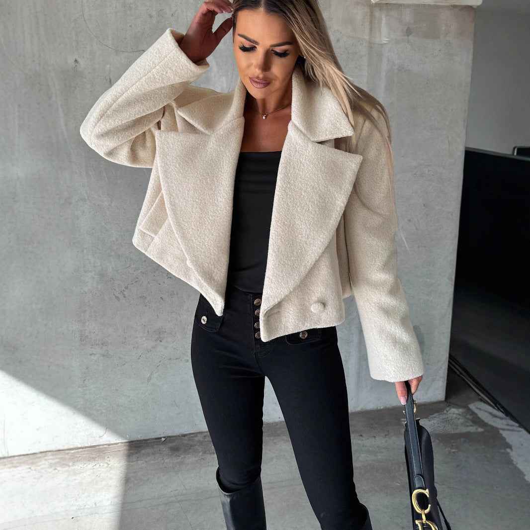Woman wearing a beige coat and black pants against a concrete wall.