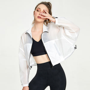 Woman wearing a white jacket over a black sports bra and leggings on a white background