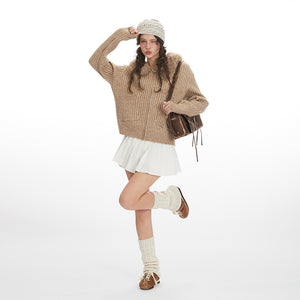 Woman wearing a beige sweater, white skirt, and brown boots on a white background