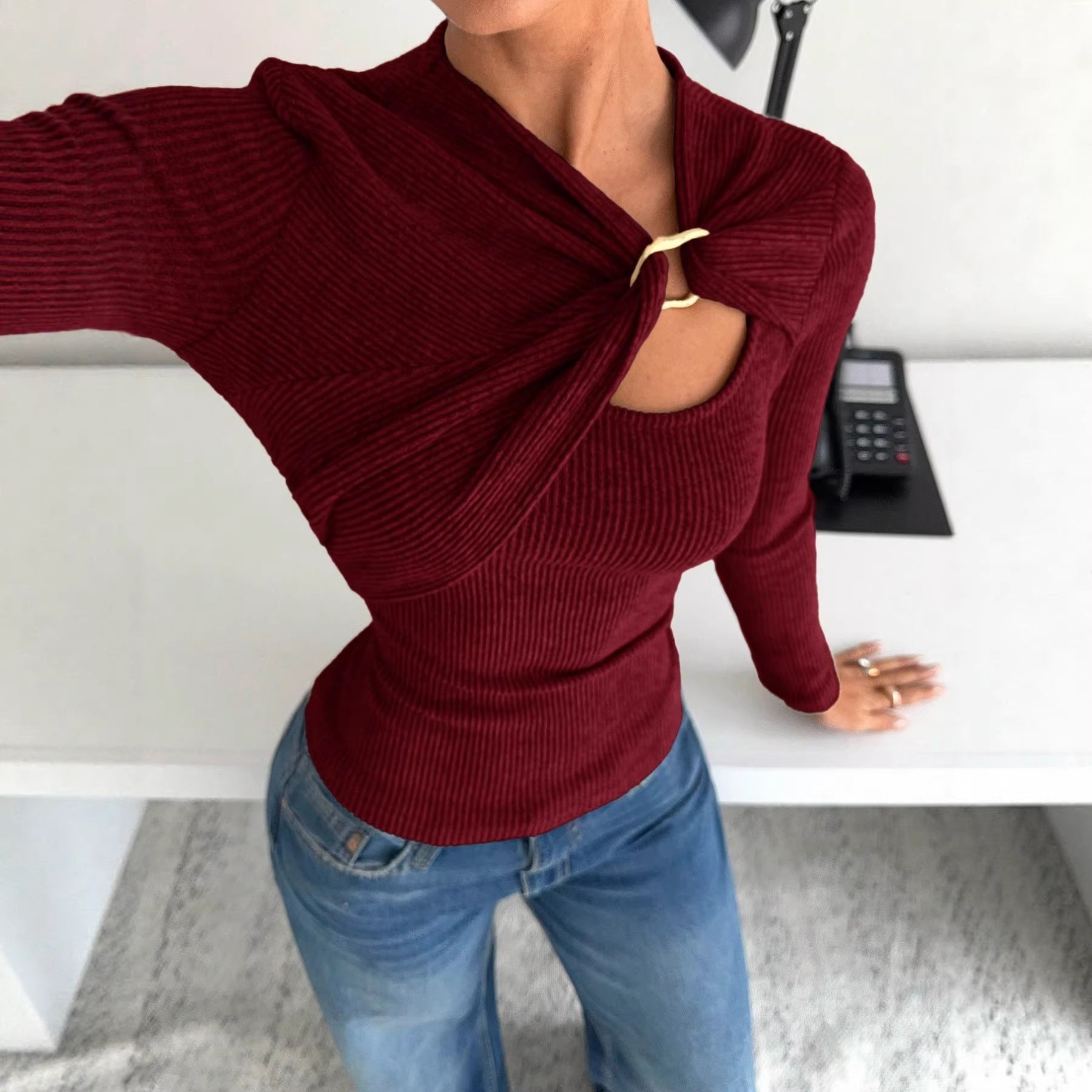 Person wearing a burgundy sweater with cut-out design and blue jeans in an office setting.