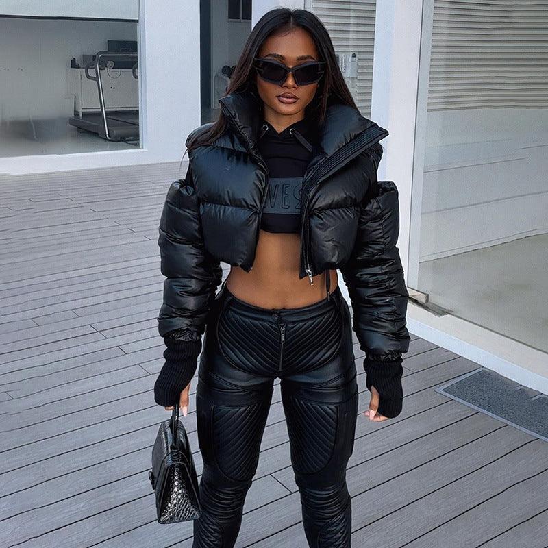 A person wearing a black, off-shoulder, hollow-out cotton jacket with zipper details and a stand-up collar, paired with black leggings. Accessories include sunglasses, a bag, and a chain.