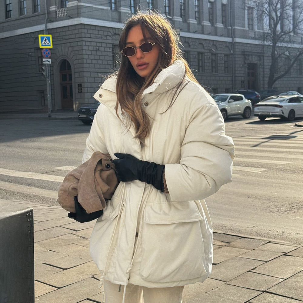 Woman in a white coat and sunglasses standing on a city street.