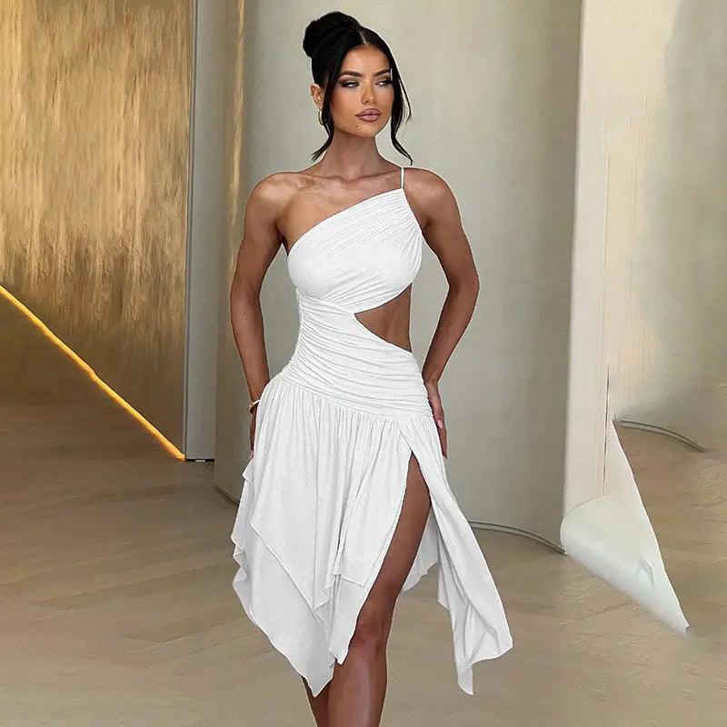 A woman wearing a white, solid color, form-fitting dress with a asymmetrical neckline and a high slit on the left side, standing in a room with a minimalist design.
