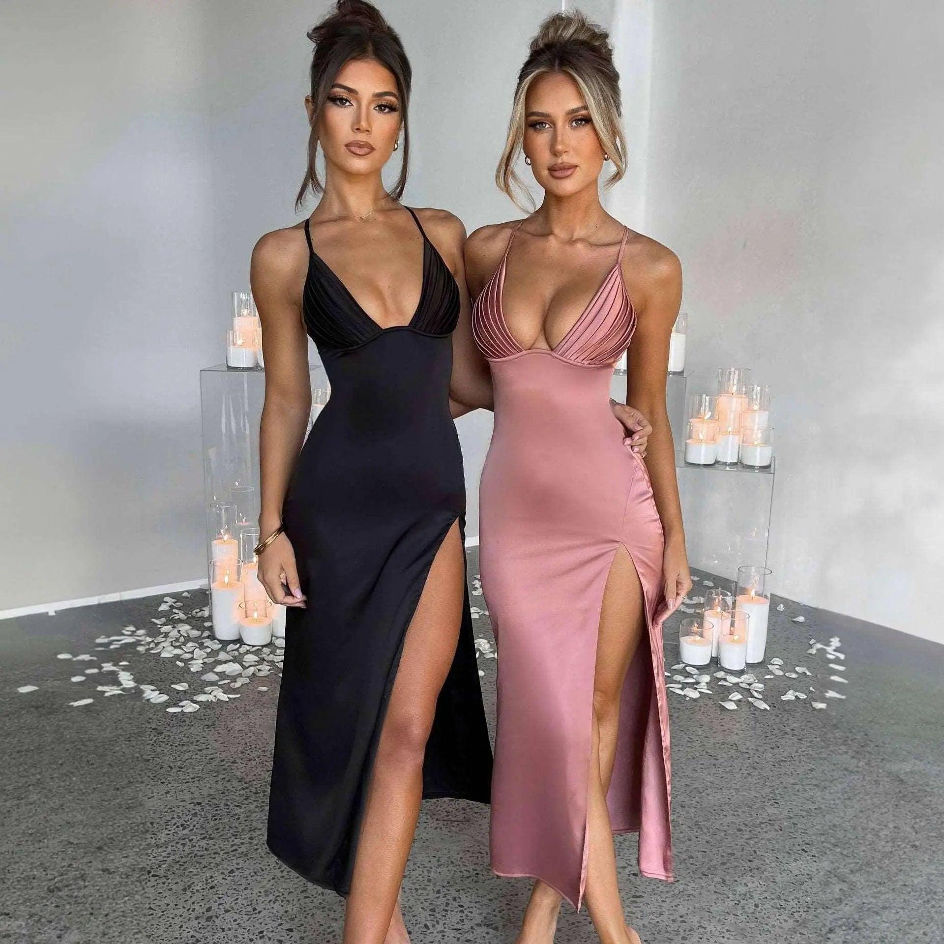 Two models wearing V-neck spaghetti strap bodycon dresses in black and pink colors, standing in a room with a grey floor and candles in the background.