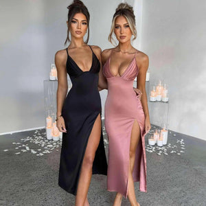 Two models wearing V-neck spaghetti strap bodycon dresses in black and pink colors, standing in a room with a grey floor and candles in the background.