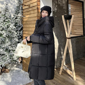 A woman wearing a mid-length hooded cotton coat in a milky white color, standing near a Christmas tree and wooden structures.