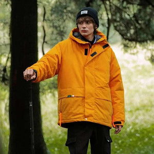 A person wearing a khaki green hooded cotton jacket with a zipper, standing in a wooded area.