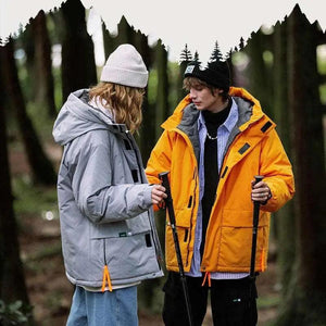 A person wearing a khaki green hooded cotton jacket with a zipper, standing in a wooded area.