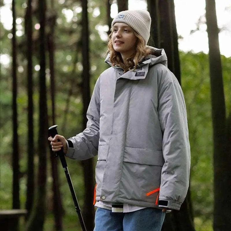 A person wearing a khaki green hooded cotton jacket with a zipper, standing in a wooded area.