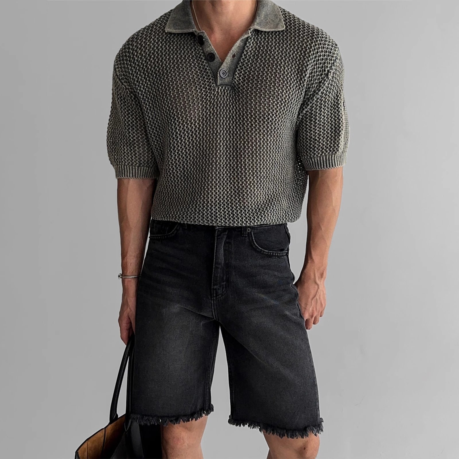 A man wearing a gray honeycomb knitted short-sleeved polo shirt with black collar, and black denim shorts.