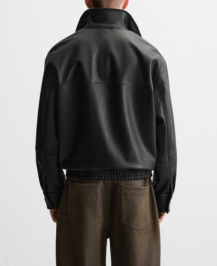 Person wearing a black leather jacket and brown pants on a white background