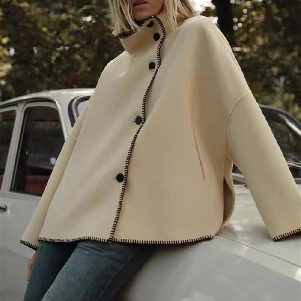 Person wearing a beige coat with black buttons sitting on a car.