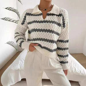 Person wearing a white and gray striped sweater with white pants in a minimalistic room.
