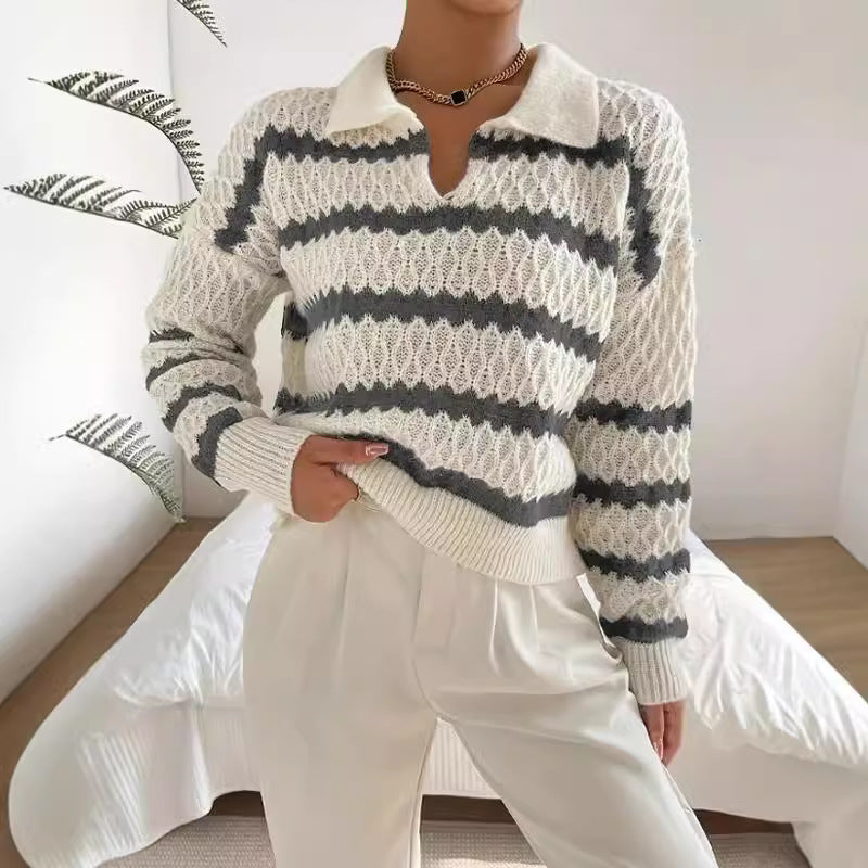 Person wearing a white and gray striped sweater with white pants in a minimalistic room.