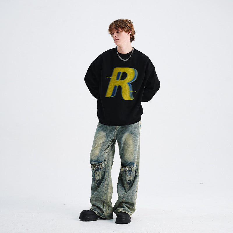 Person wearing a black sweater with a yellow 'R' logo and blue jeans on a white background