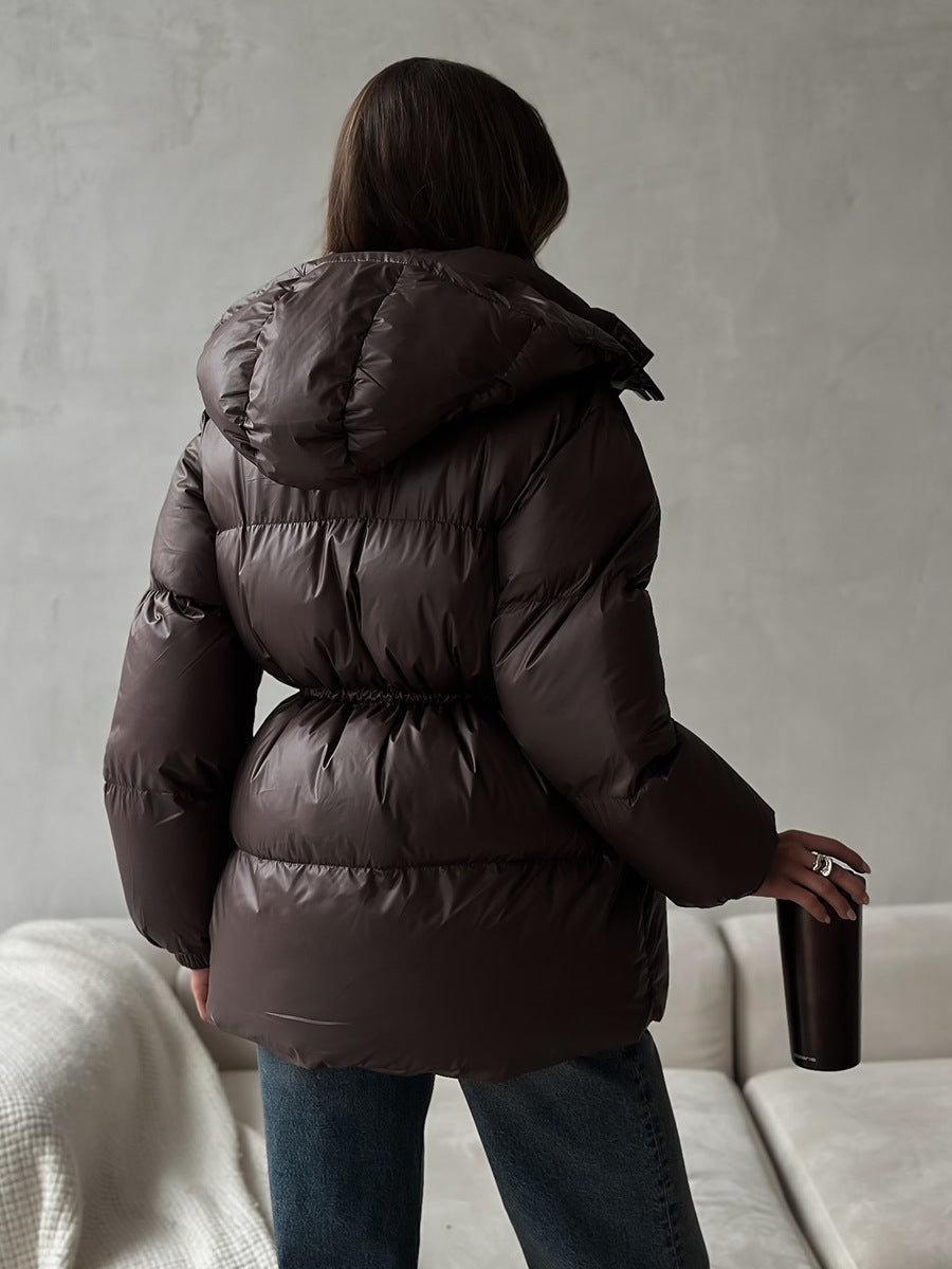 Person wearing a dark brown puffer jacket holding a bottle against a neutral background