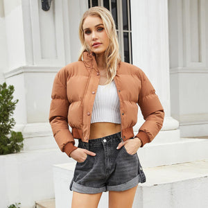 A woman wearing a short high-collar warm coat in brown color, paired with a white top and denim shorts.