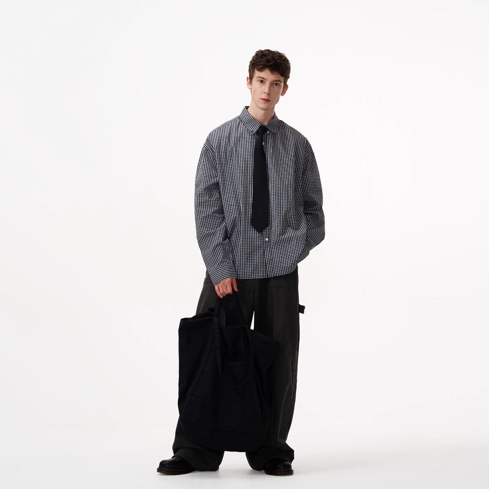 Person wearing a checkered shirt and black pants on a white background