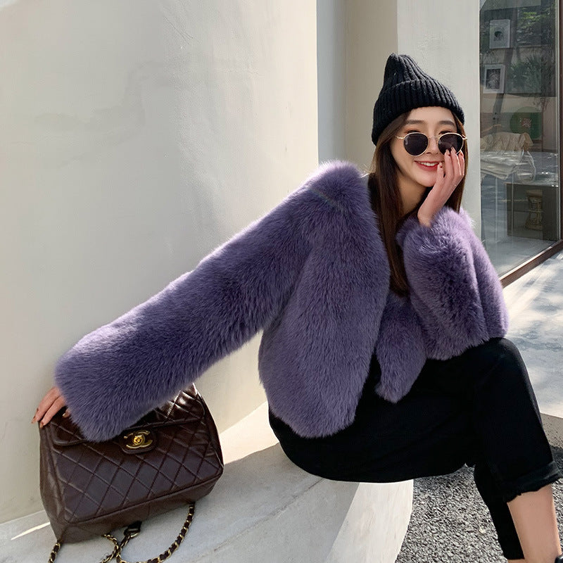 Woman wearing a purple fur coat and black beanie sitting on a stone ledge.
