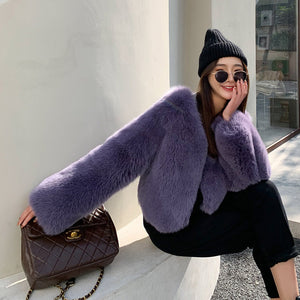 Woman wearing a purple fur coat and black beanie sitting on a stone ledge.