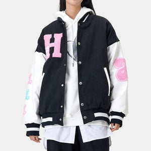 A person wearing a casual baseball jacket with a bear pattern, the jacket is primarily black with blue and apricot options, paired with a white hoodie and a t-shirt.