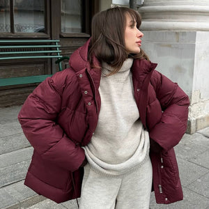Woman wearing a maroon puffer jacket over a beige sweater and pants on a city street.