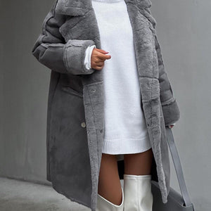 A woman wearing a long gray suede cardigan coat with a plush suit collar and metal details, paired with a white dress and white boots.