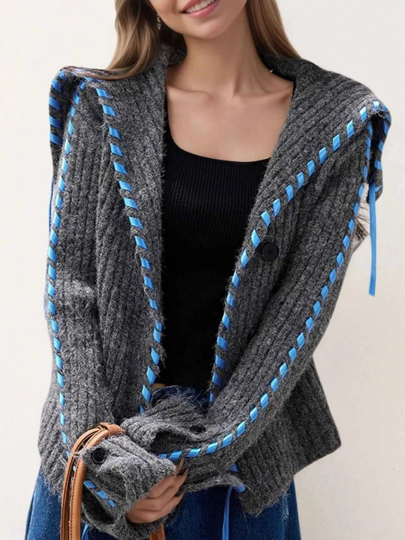 Person wearing a gray cardigan with blue accents on a plain background