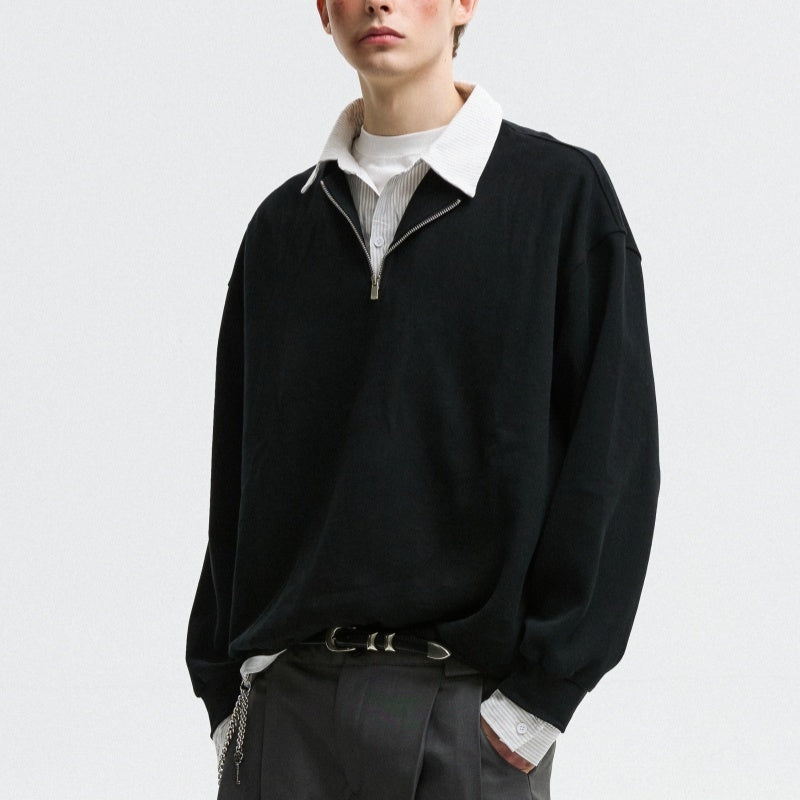 Person wearing a black sweater over a white shirt with gray pants on a light gray background