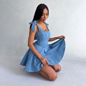 Woman wearing a blue dress with bow straps on a plain background