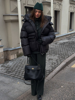 Person wearing a black puffer jacket and green beanie walking on a street.