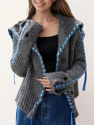 Woman wearing a gray knitted cardigan with blue accents on a plain background