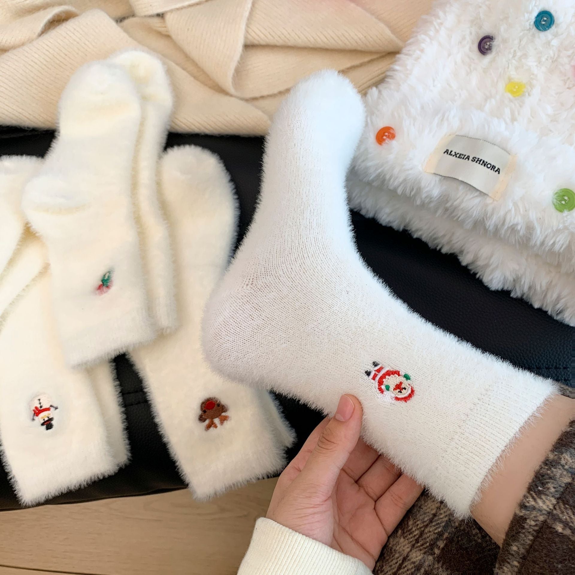 White socks with embroidered designs held by a hand, with more socks in the background.