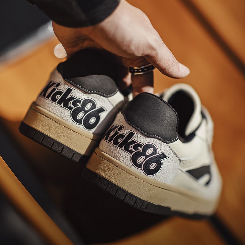 Pair of 'Kicks86' sneakers held by a hand on a wooden surface